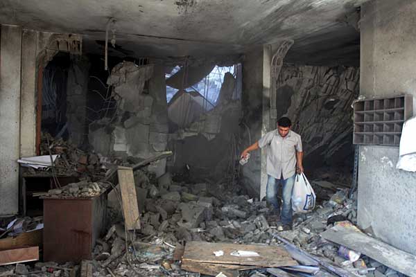 A man gathers his belongings that survived after an Israeli bomb was dropped on his home. Photo courtesy of rinf.com. 